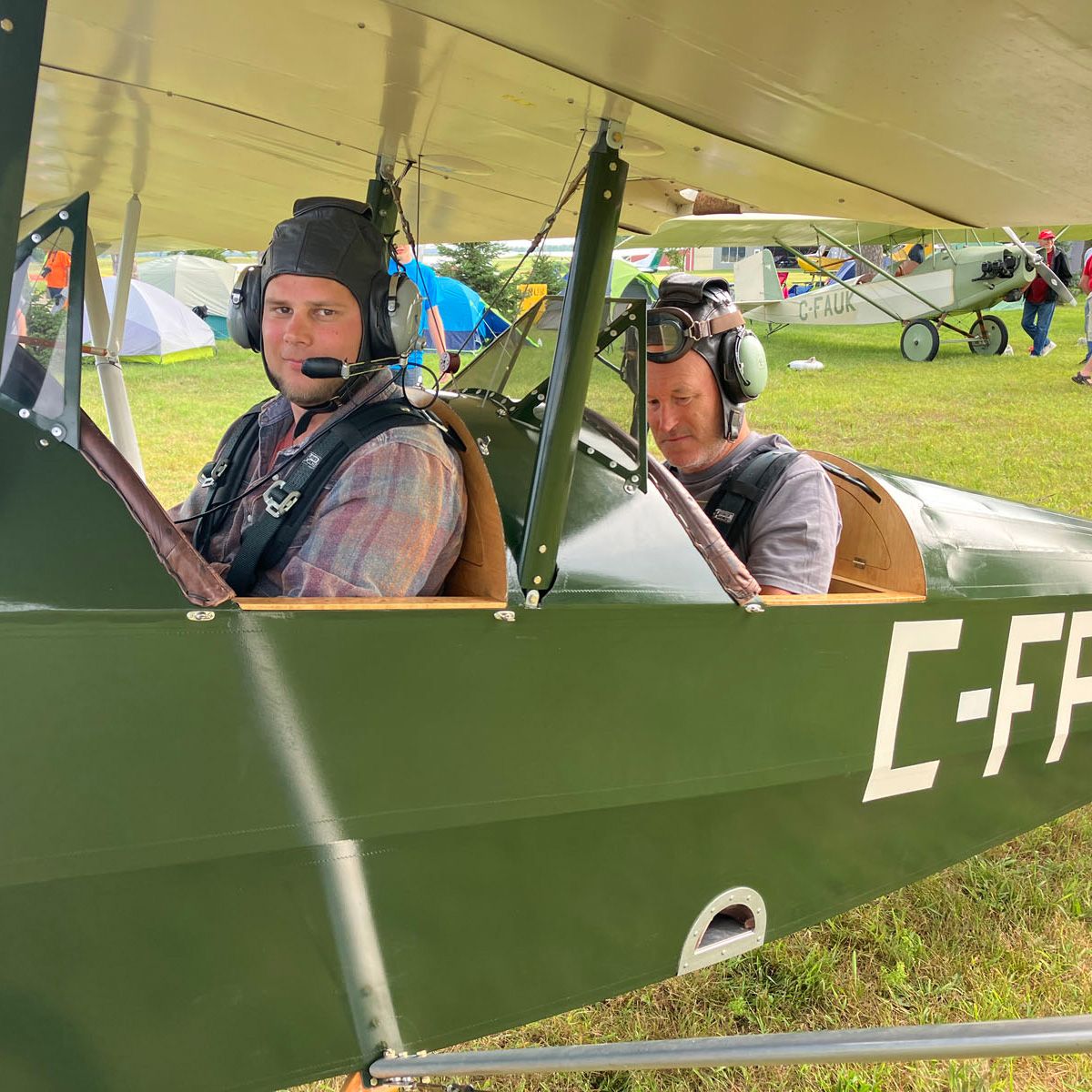 close up of two men in a green open-cockpit plane