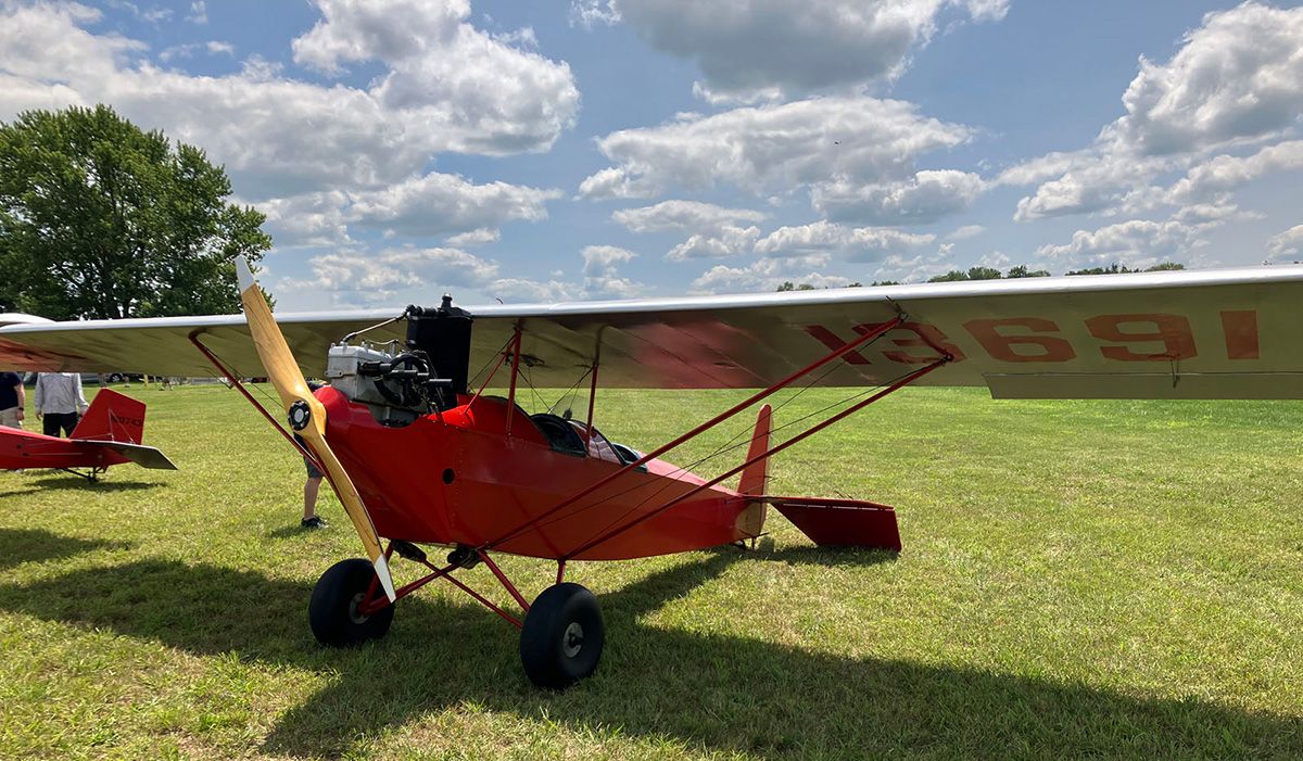 red pietenpol parked under grass under pretty clouds and blue sky