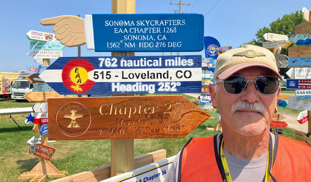 darrel in orange vest standing in front of sign that has sonoma skycrafters 1562 NM with a pointing hand, and two more signs for other chapters