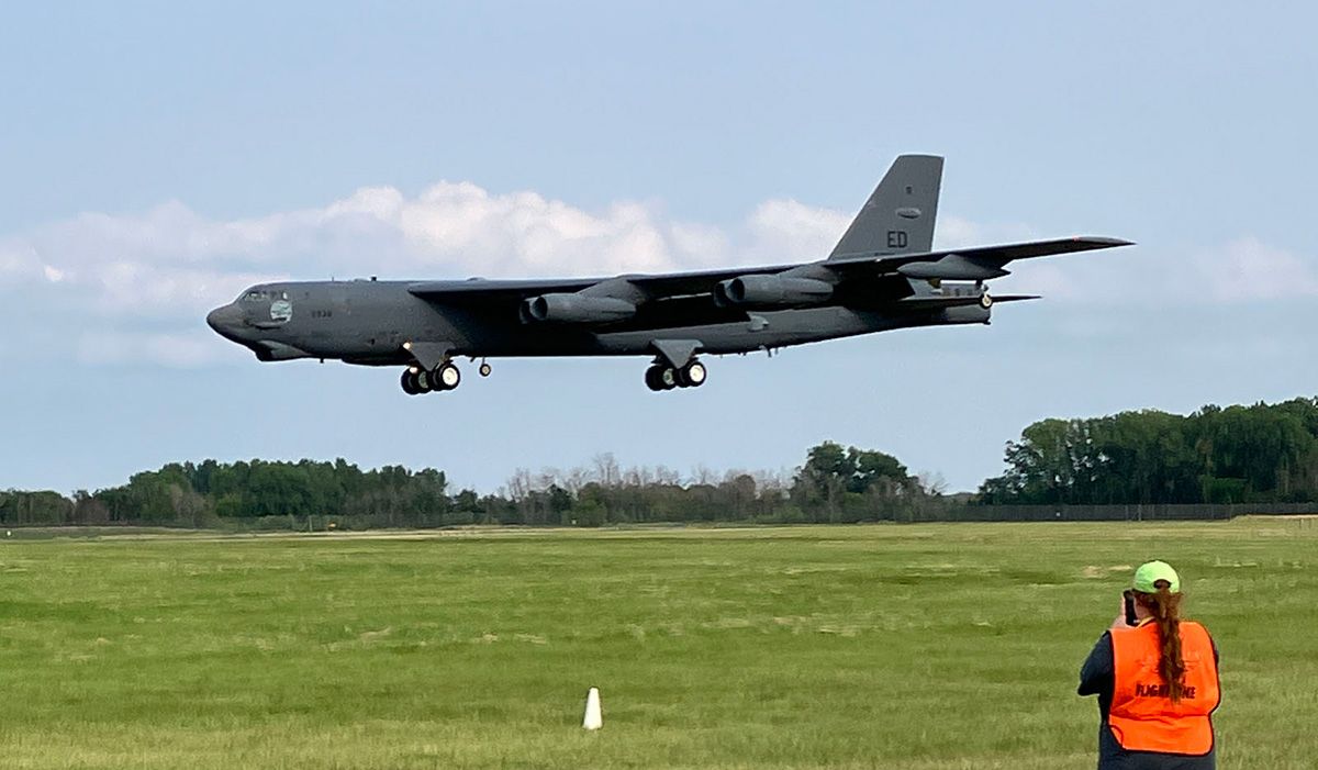 large military plane landing at oshkosh, woman in orange vest in foreground