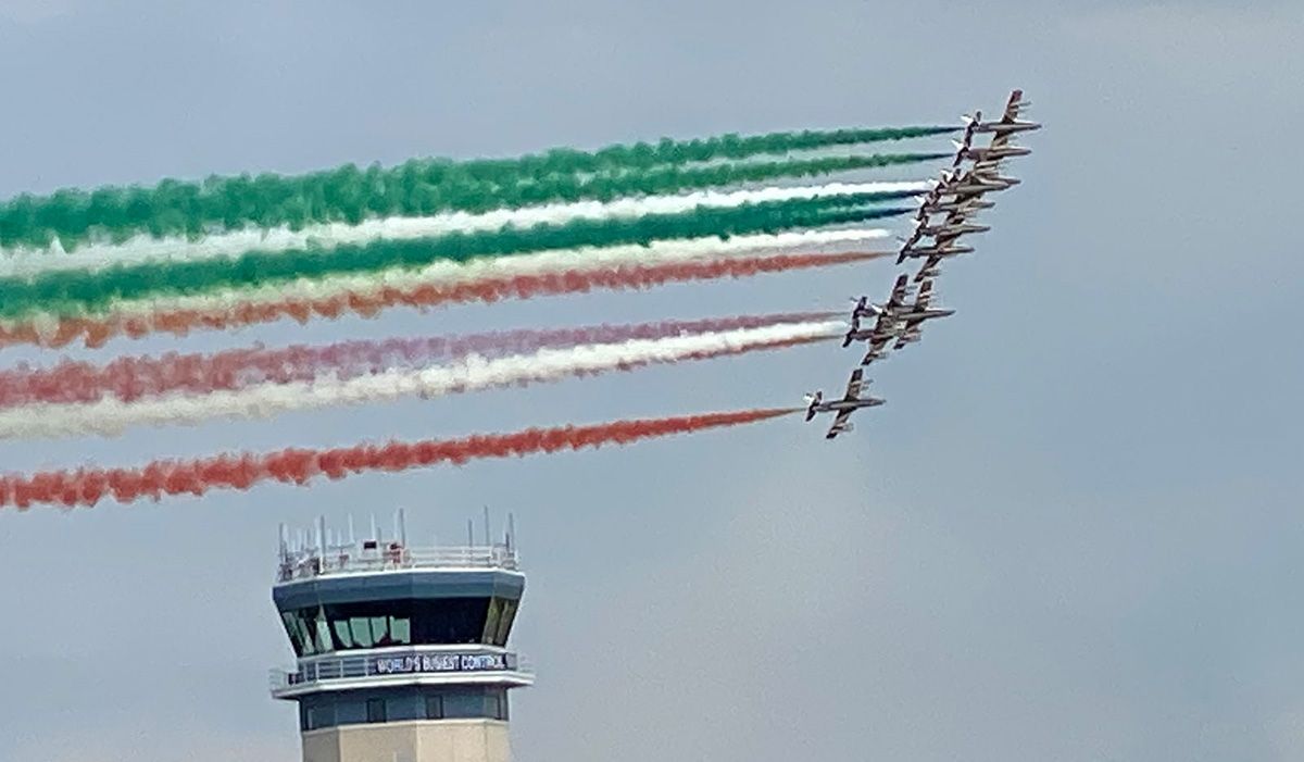 planes trailing red, white, and green smoke flying over air traffic tower